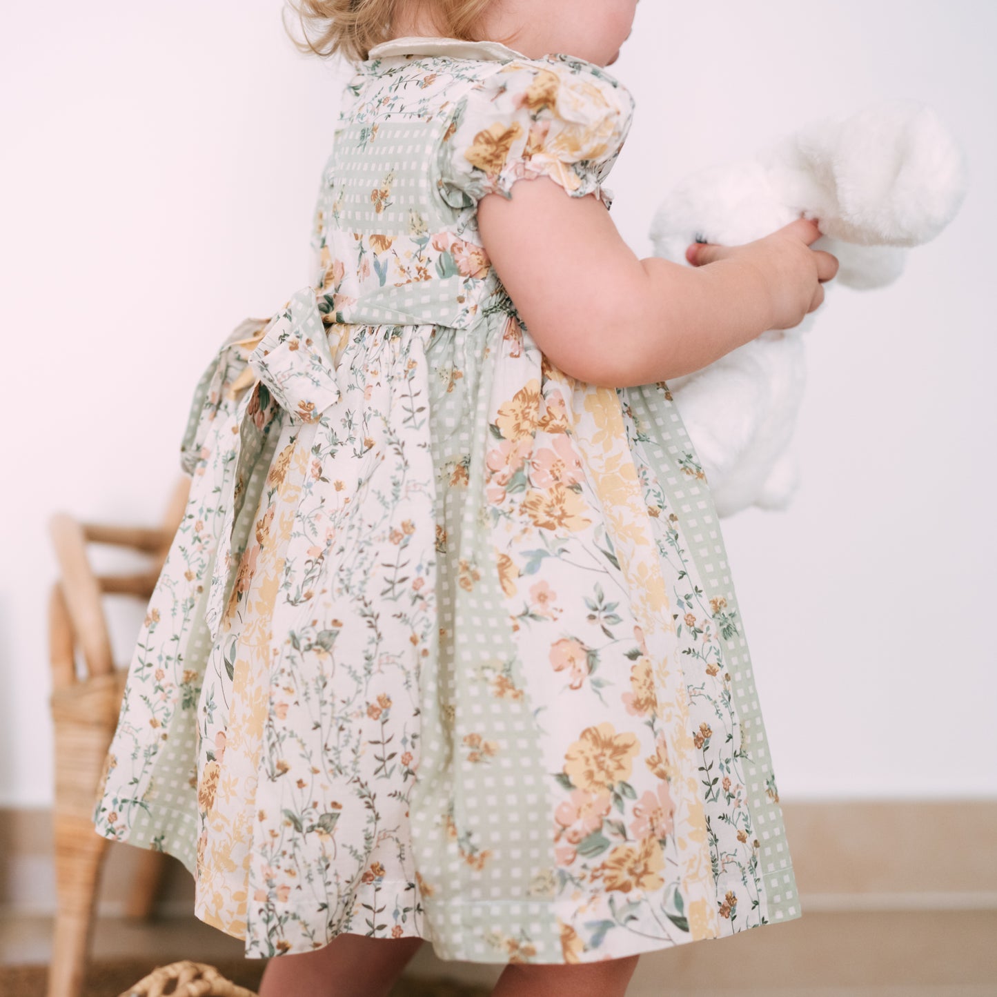 Toddler wearing a pastel floral dress and matching hair accessory, cuddling a white stuffed bunny toy.