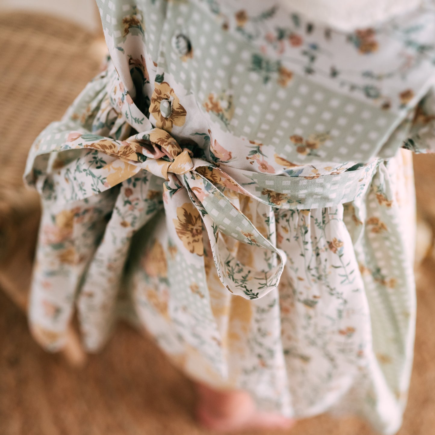 Close-up of a floral dress back tie bow detail in soft pastel tones with buttons and delicate floral prints.